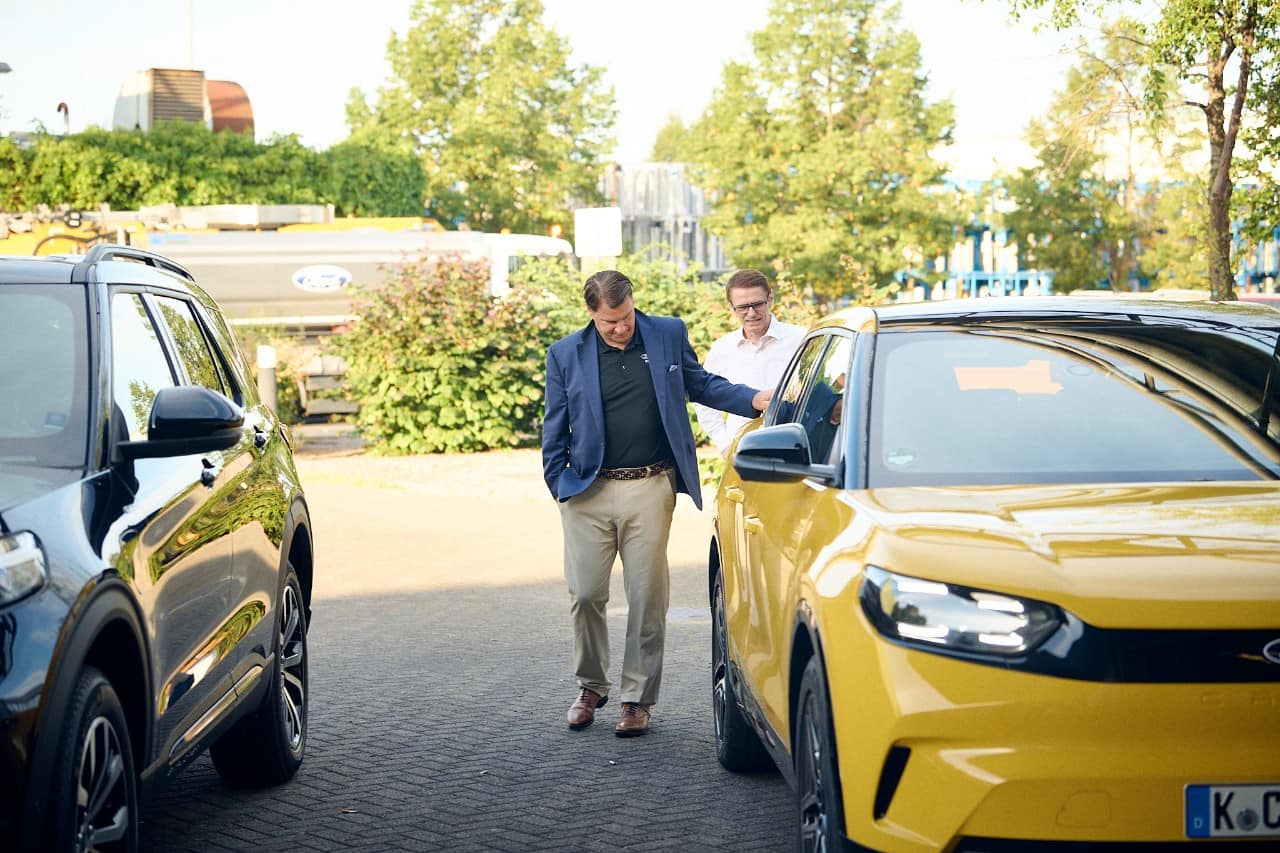 Jim Farley dressed in khaki pants and a blue blazer looks at a yellow Ford Capri.